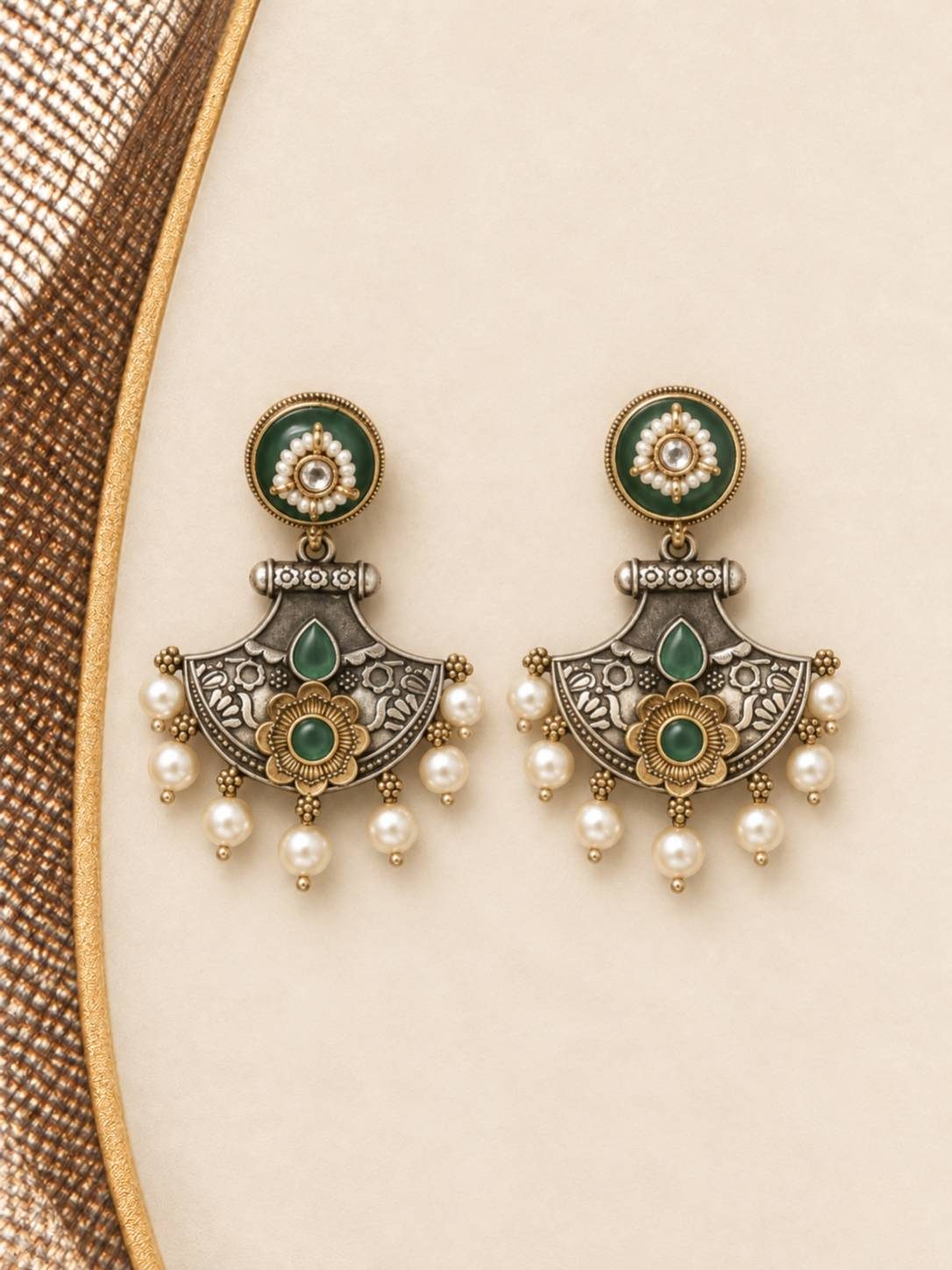 Close-up flat lay of matching dual-tone chandbali earrings with green stones and pearl drops