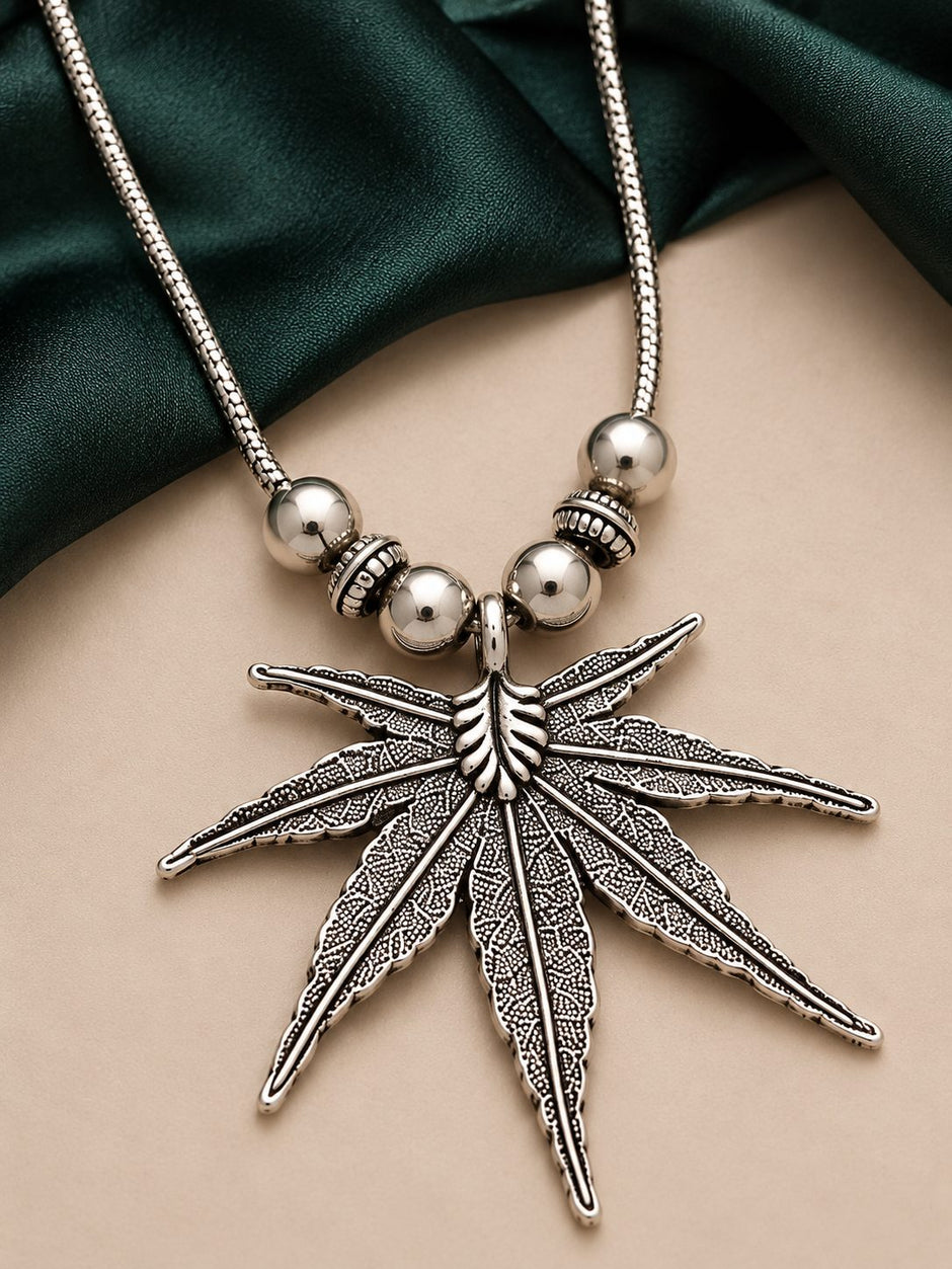 Close-up of oxidised silver cannabis leaf pendant with textured detailing and polished ball bead accents on snake chain