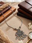 Oxidised silver necklace with floral peacock pendant styled on linen beside leather journals