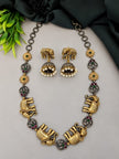 Dual-tone elephant motif necklace and jhumka earring set laid flat on a grey surface with green leaves