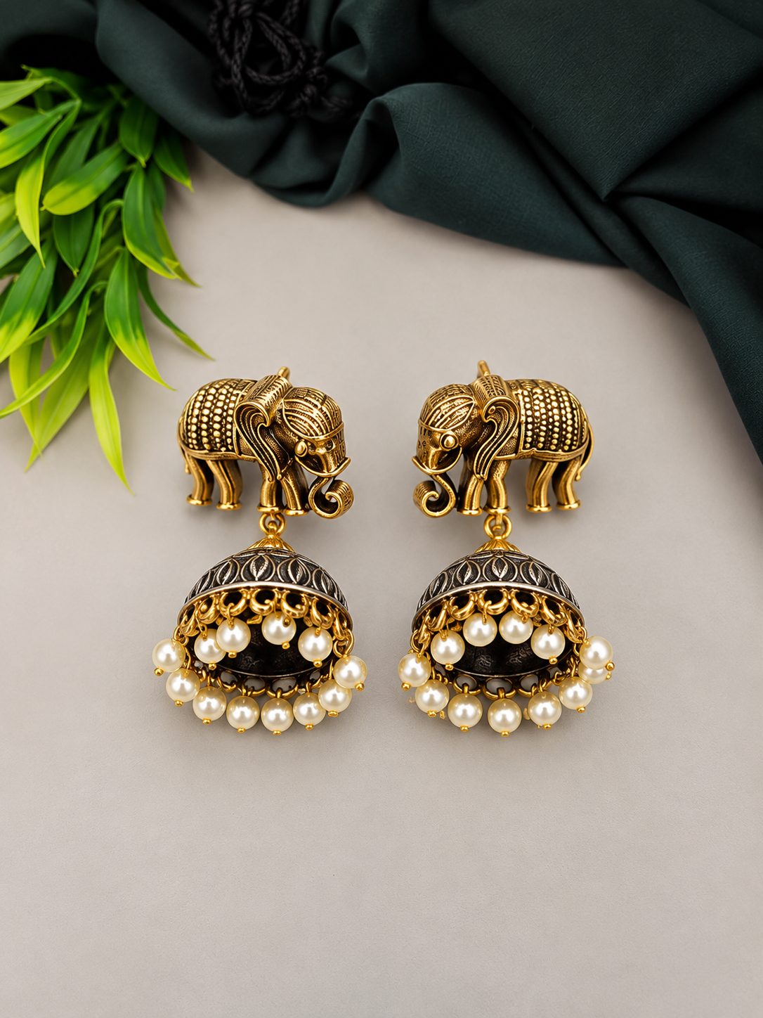 Close-up of oxidised gold elephant stud jhumka earrings with pearl drops on grey background