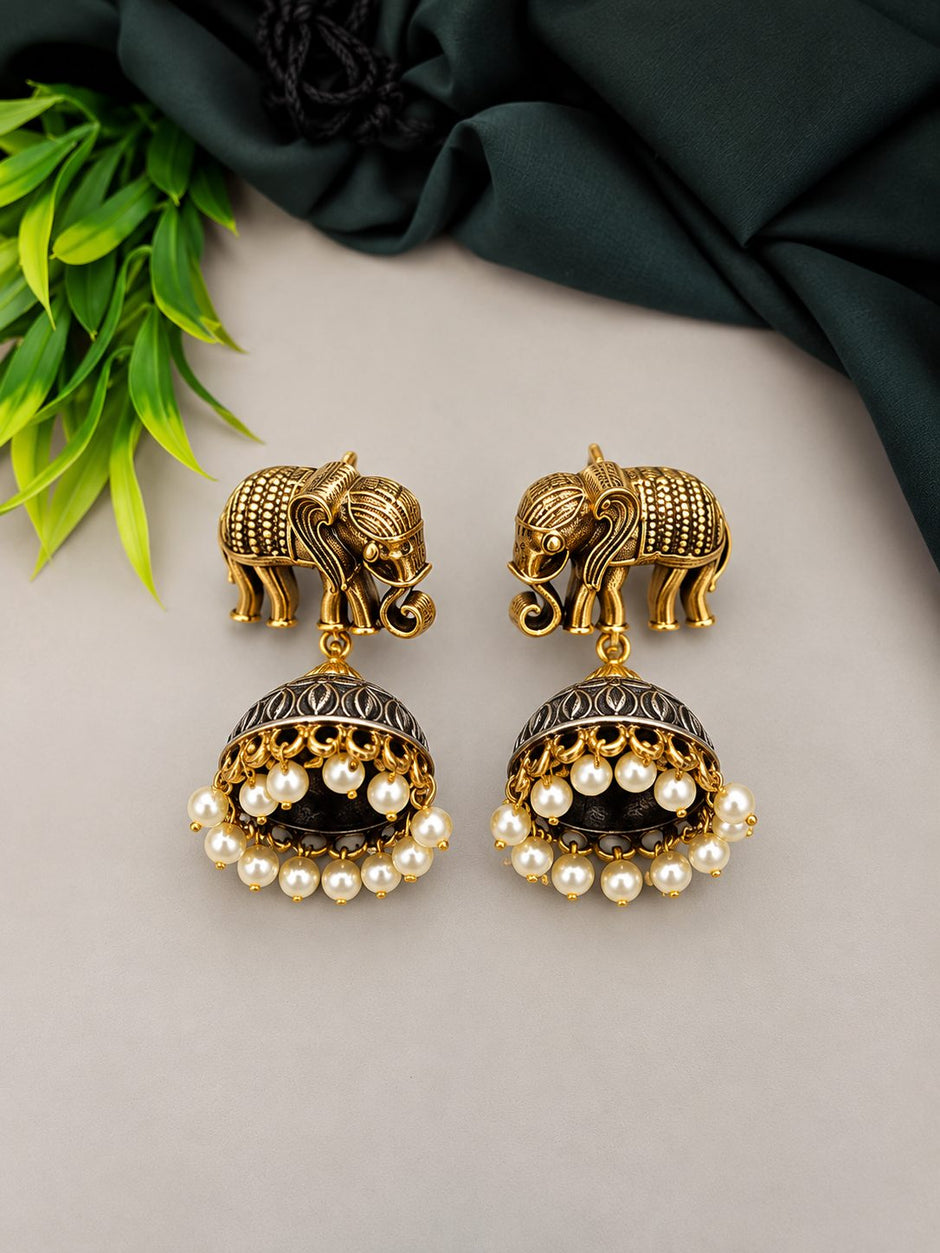 Close-up of oxidised gold elephant stud jhumka earrings with pearl drops on grey background