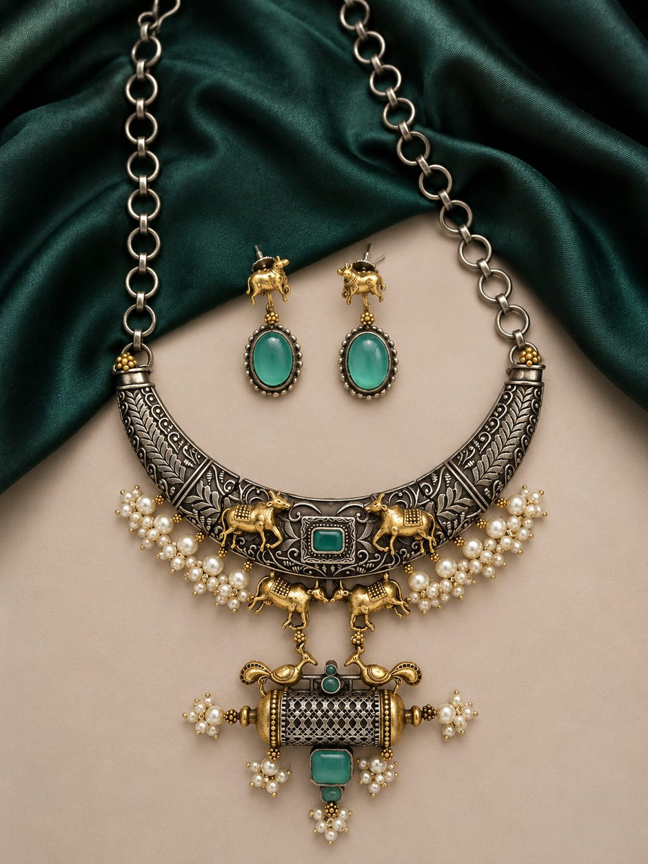Oxidised silver dual-tone choker necklace set with pearl drops and green stones on a beige surface with dark green silk