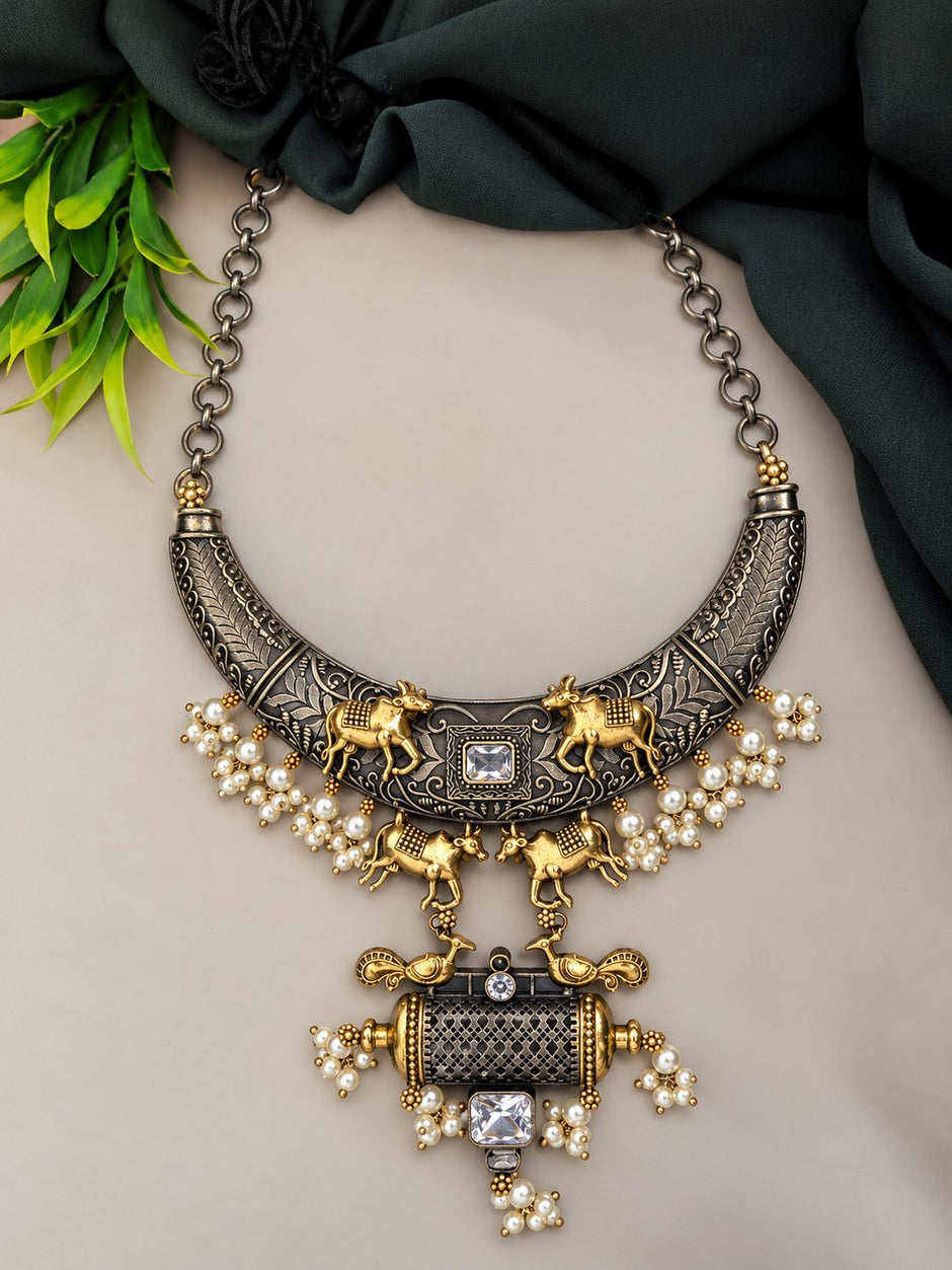 Flat lay of oxidised crescent collar necklace with pearl clusters and cylindrical crystal pendant on neutral background
