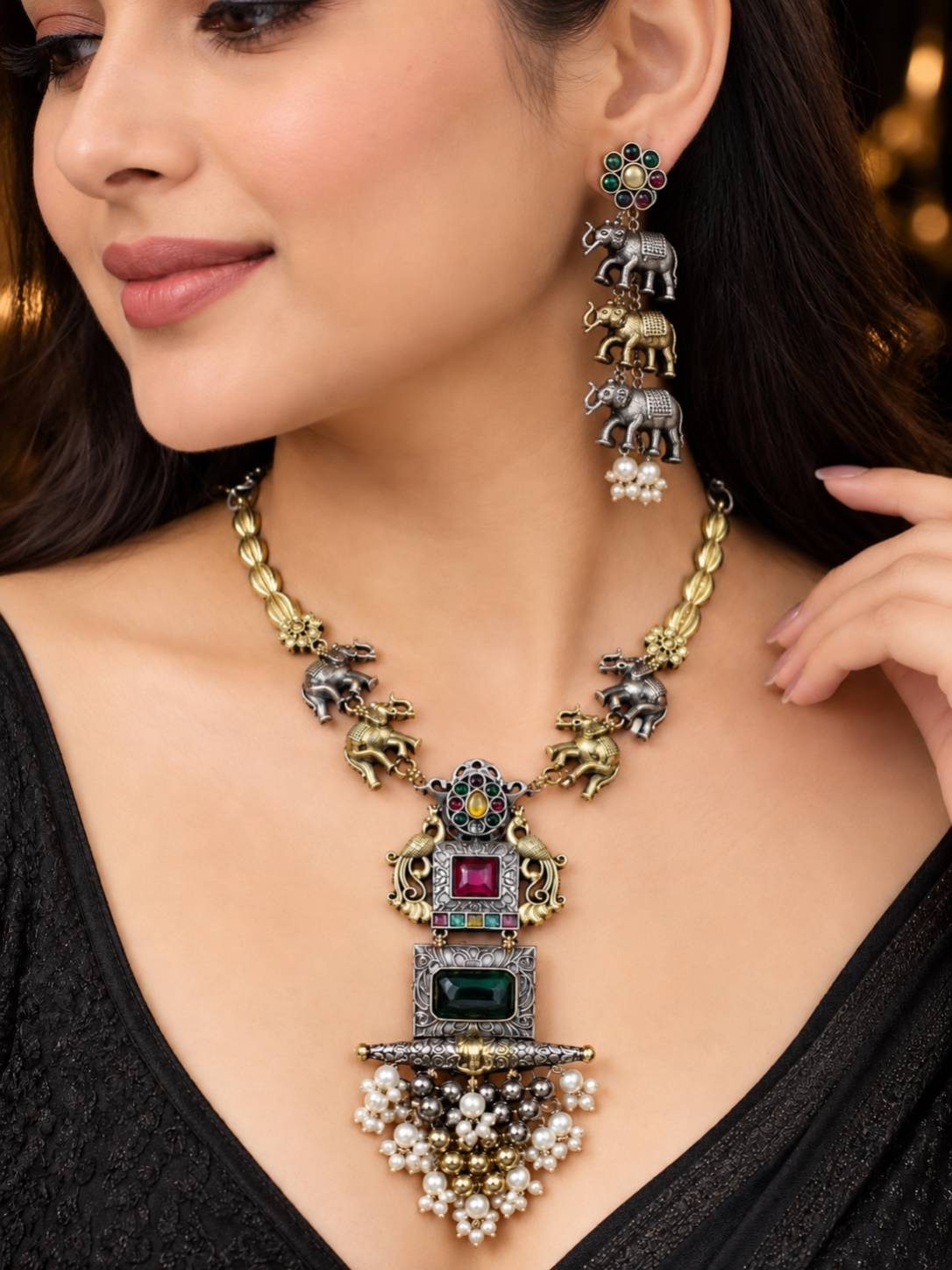 Woman wearing oxidised elephant necklace with ruby stone pendant and triple elephant earrings against dark background