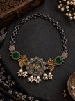 Dual-tone oxidised peacock choker with green stones and pearl drops laid flat on dark slate surface