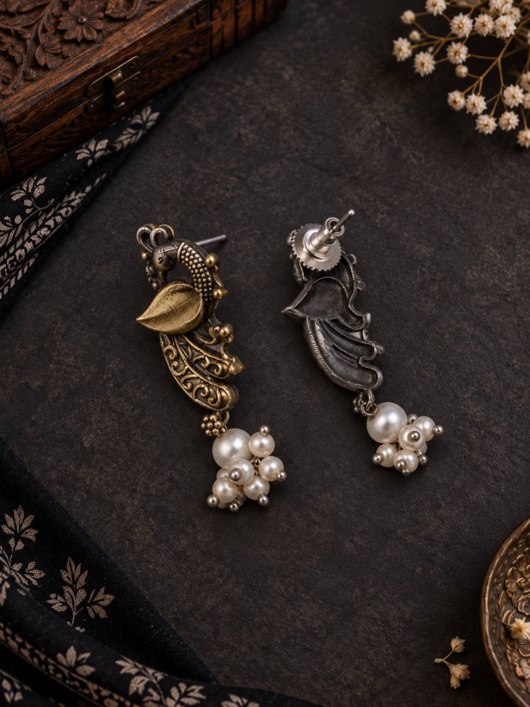 Front and back view of oxidised peacock stud earrings with pearl drops on dark stone surface