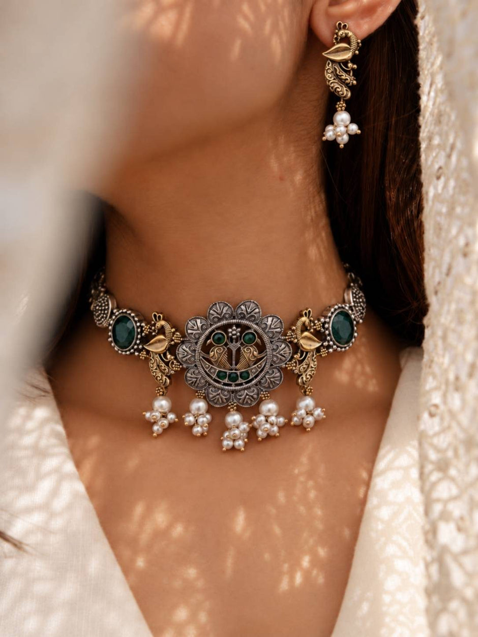Woman wearing oxidised peacock choker necklace and earrings with a white embroidered outfit