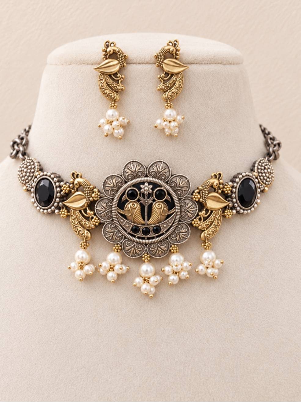 Oxidised dual-tone peacock choker necklace and drop earrings displayed on a cream velvet jewellery stand