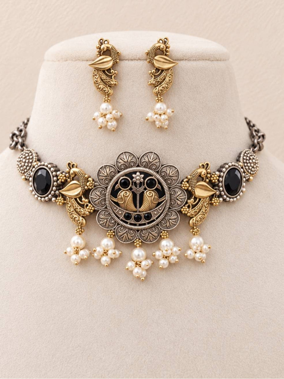 Oxidised dual-tone peacock choker necklace and drop earrings displayed on a cream velvet jewellery stand