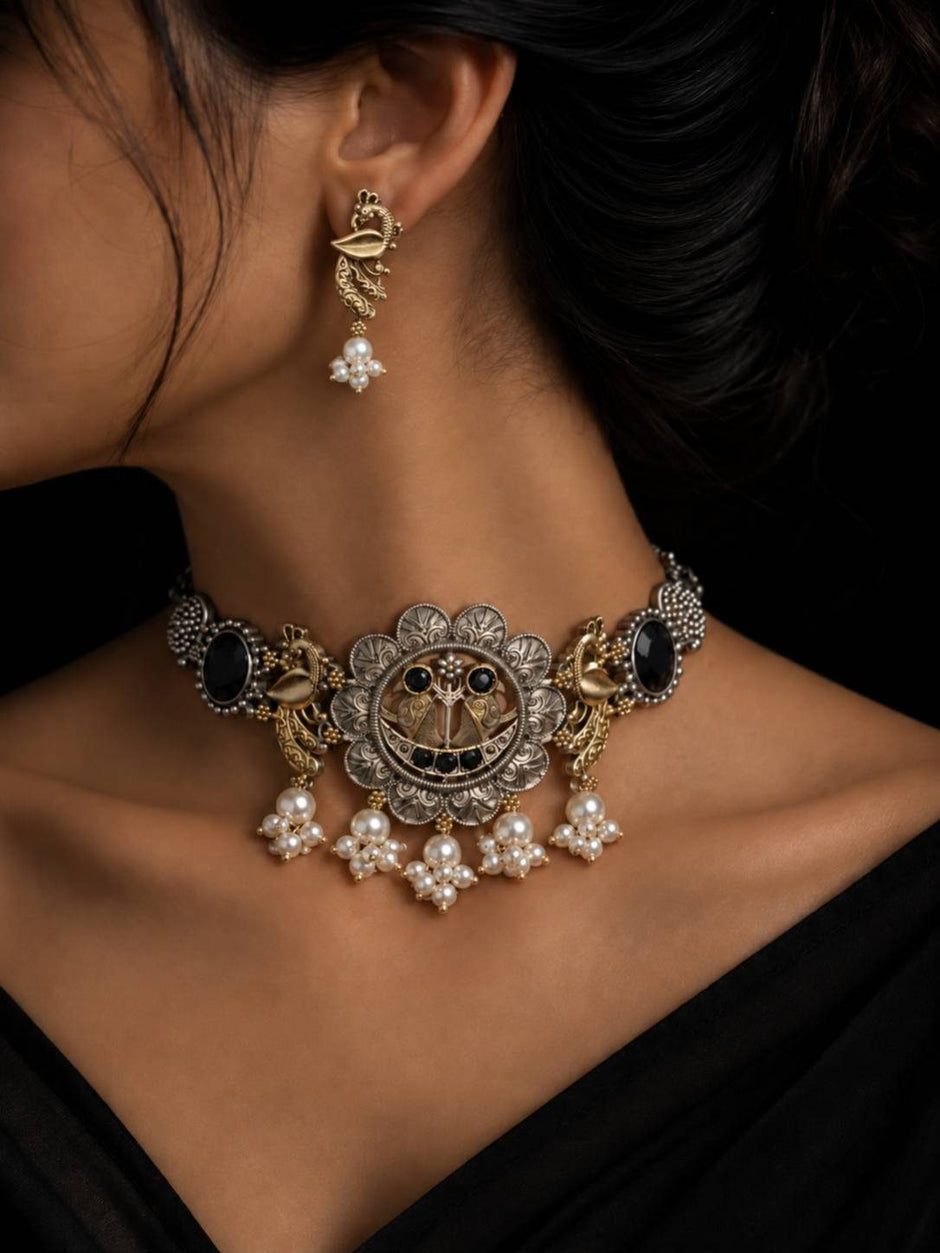 Woman wearing oxidised peacock choker necklace and matching earring against a black outfit