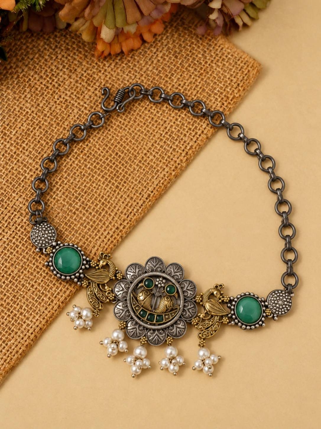 Flat lay of oxidised peacock choker necklace with green cabochons and pearl drops on burlap fabric