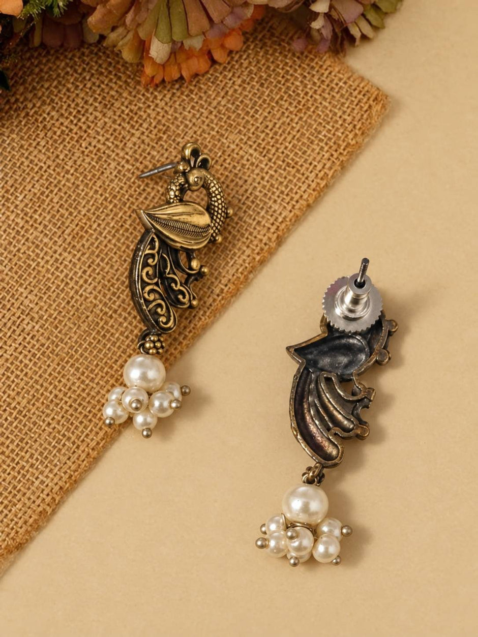 Front and back view of dual-tone peacock stud earrings with faux pearl cluster drops on burlap