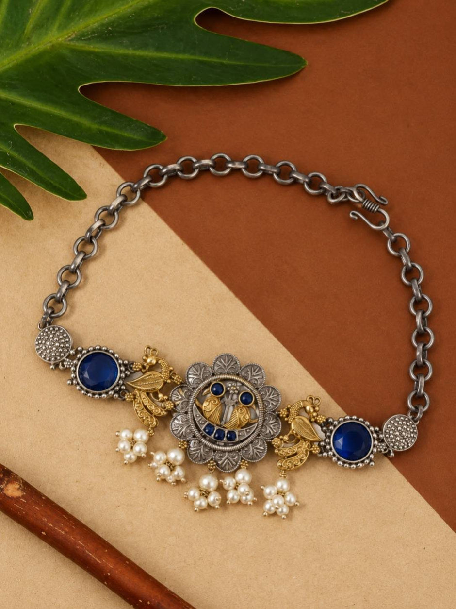 Oxidised silver peacock choker with blue glass stones and faux pearl clusters laid flat on kraft paper