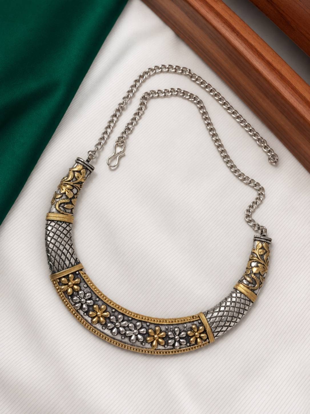 Dual-tone oxidised choker necklace laid flat on white cloth showing floral motifs and adjustable curb chain