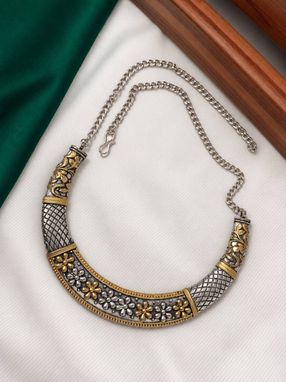Dual-tone oxidised choker necklace laid flat on white cloth showing floral motifs and adjustable curb chain