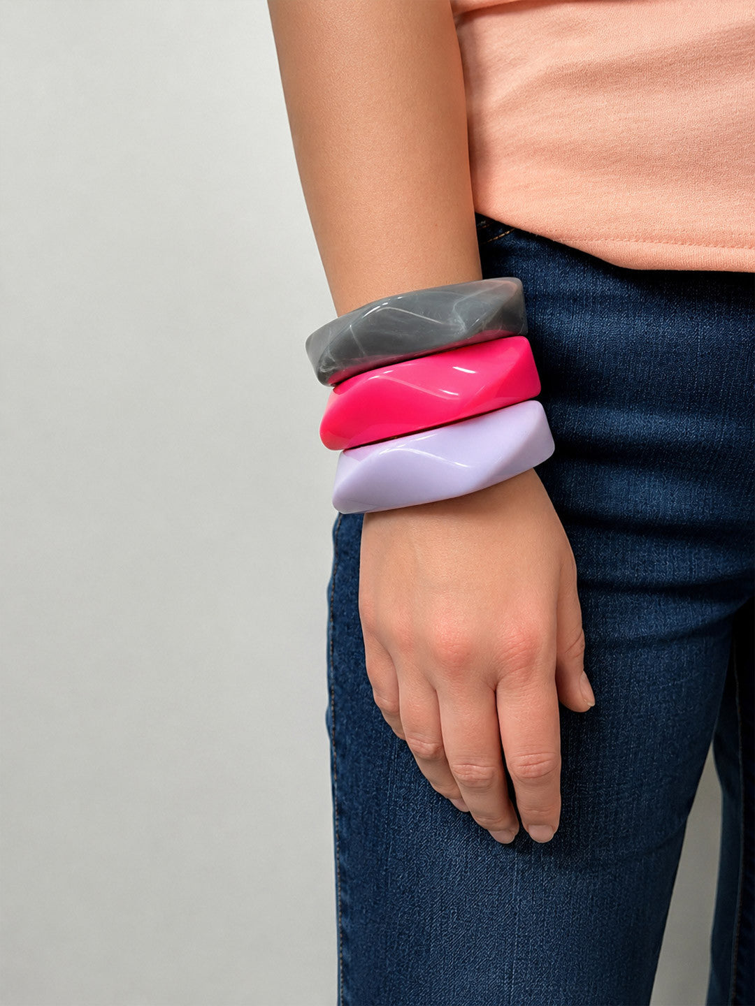 All three resin bangles stacked on a wrist styled with a peach top and dark blue jeans showing the wearable scale