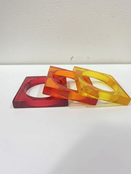 Three translucent square resin bangles in red, amber, and yellow laid flat overlapping each other on a white surface