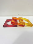Three translucent square resin bangles in red, amber, and yellow laid flat overlapping each other on a white surface