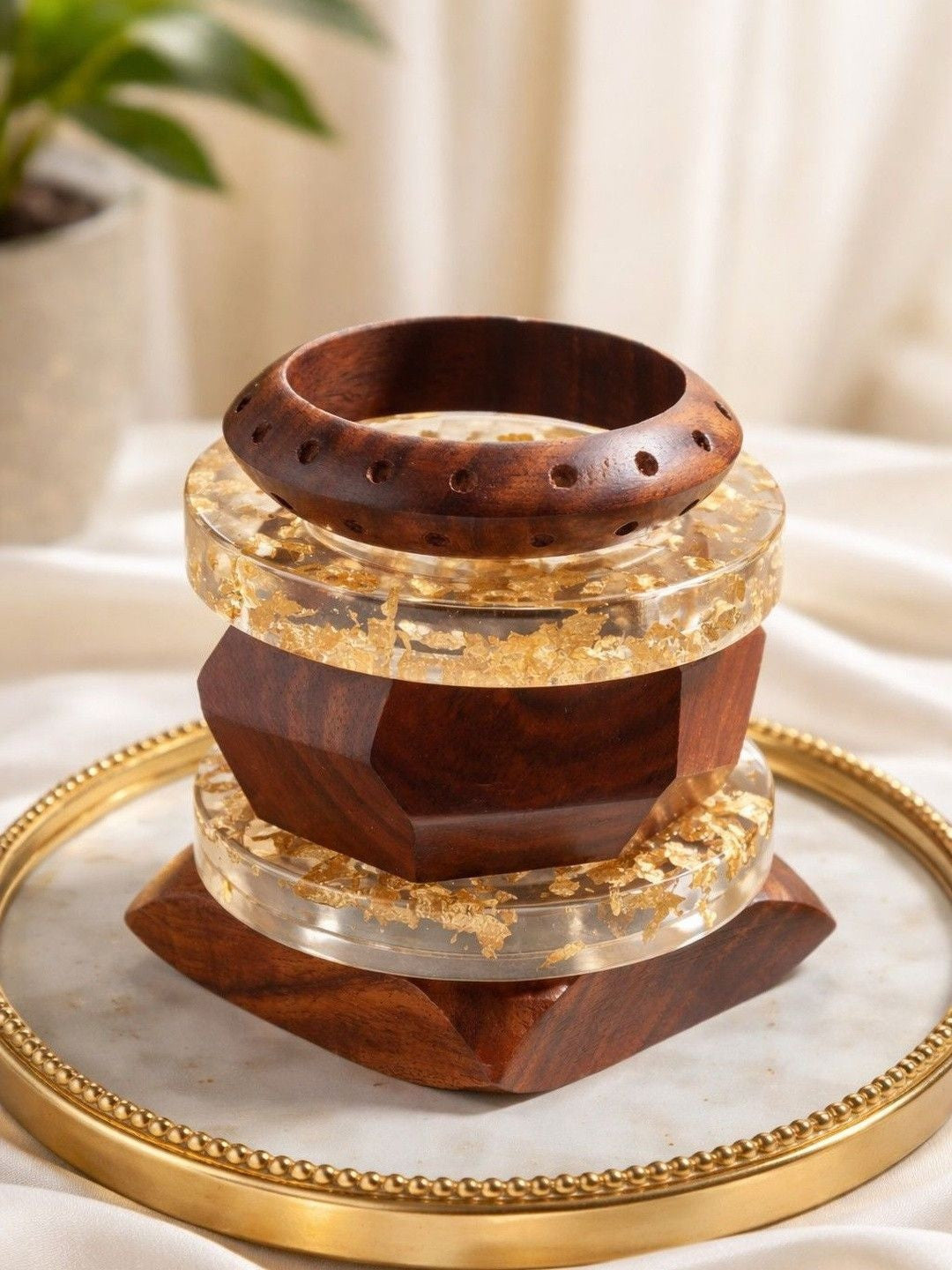 Stack of three wood and gold foil resin bangles displayed on a gold-rimmed tray with draped white fabric background