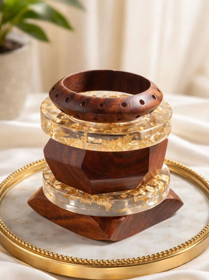 Stack of three wood and gold foil resin bangles displayed on a gold-rimmed tray with draped white fabric background