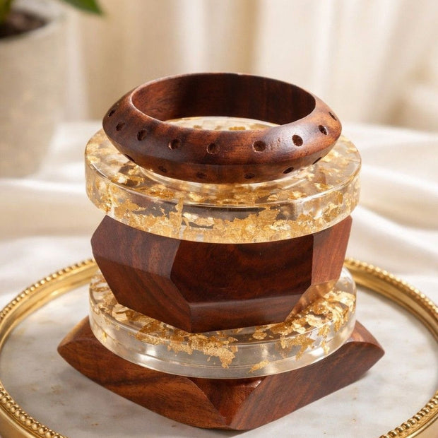 Stack of three wood and gold foil resin bangles displayed on a gold-rimmed tray with draped white fabric background