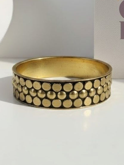 Gold-tone rigid bangle with raised circular dot pattern and darkened oxidised base, photographed flat on white surface