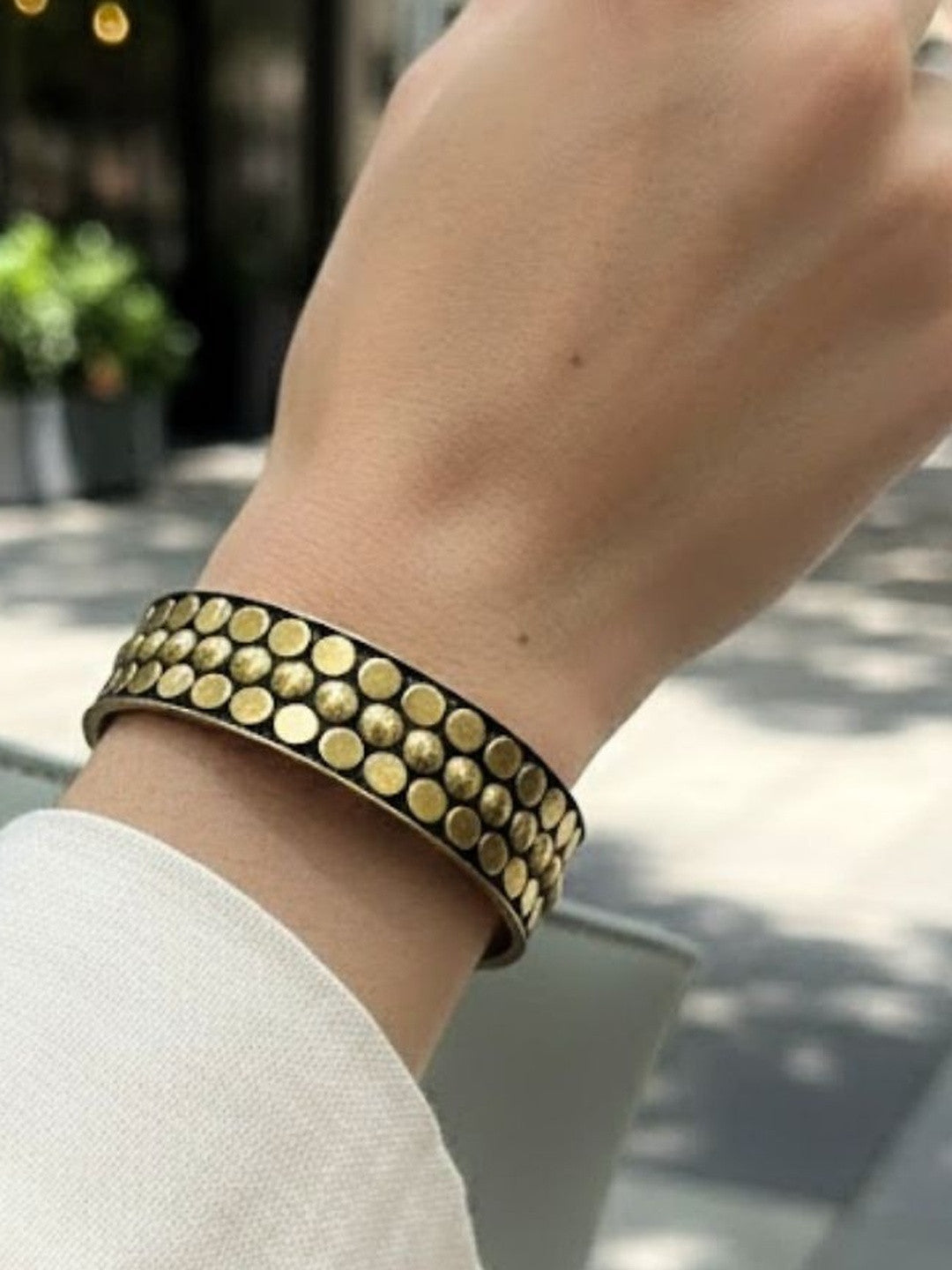 Antique gold studded cuff bangle worn on a woman's wrist over a white full-sleeve top, shown outdoors