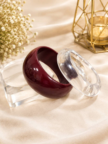 Clear and maroon acrylic dome bangles placed separately on a crystal stand over cream satin fabric