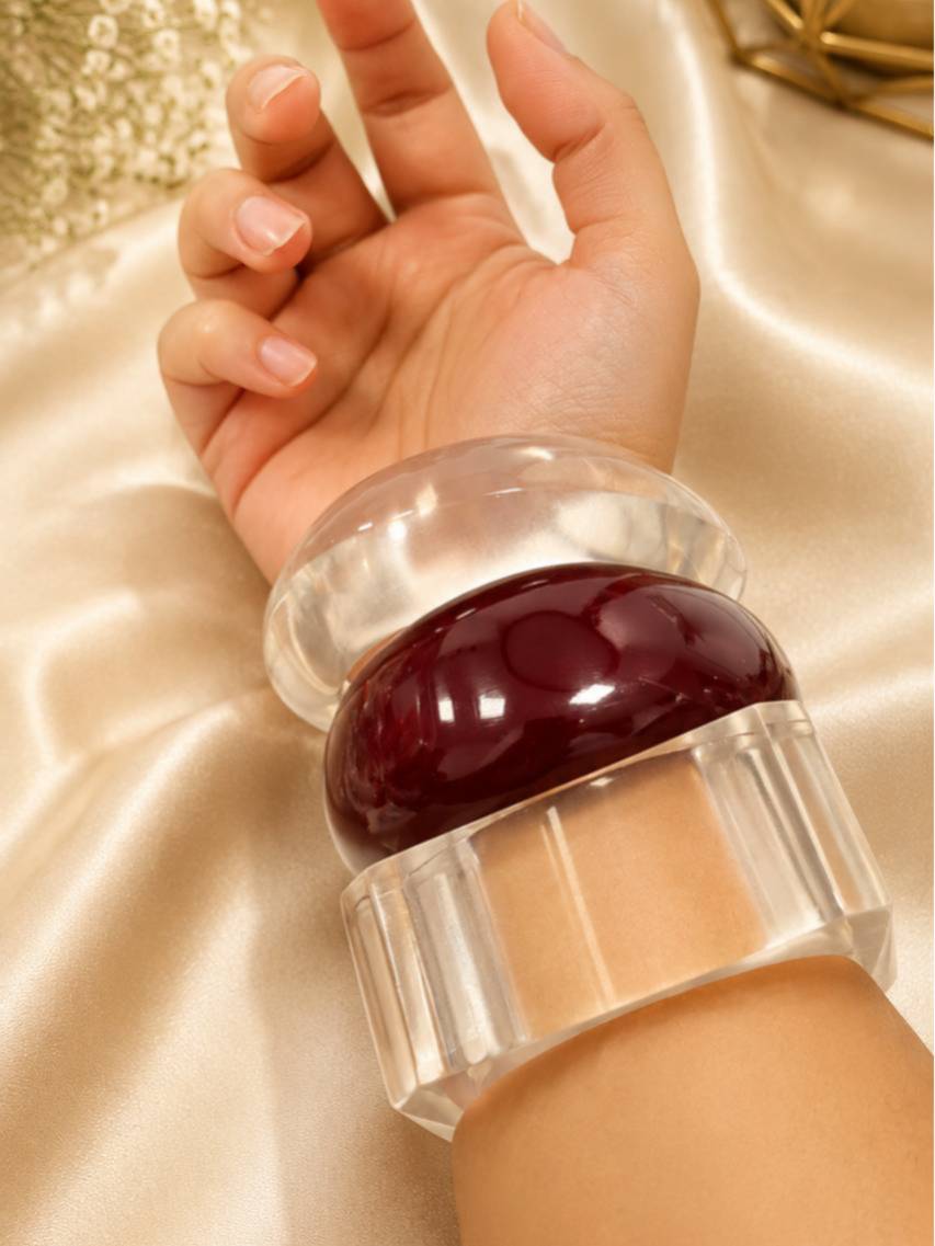 Clear and maroon acrylic dome bangles stacked and worn together on a woman's wrist over satin