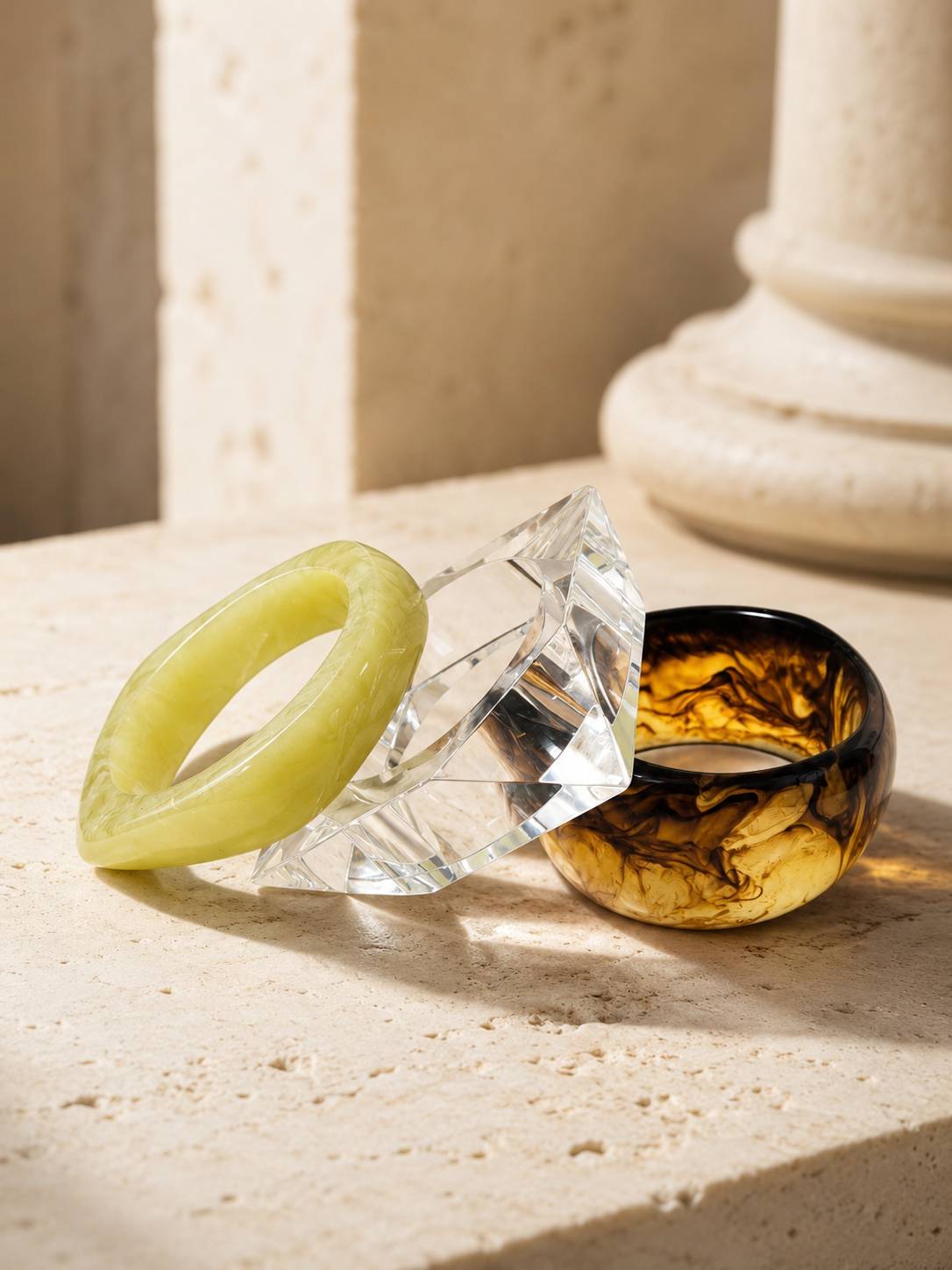 Three stacked resin bangles on travertine surface near stone column in natural light