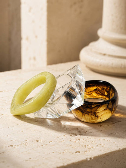 Three stacked resin bangles on travertine surface near stone column in natural light