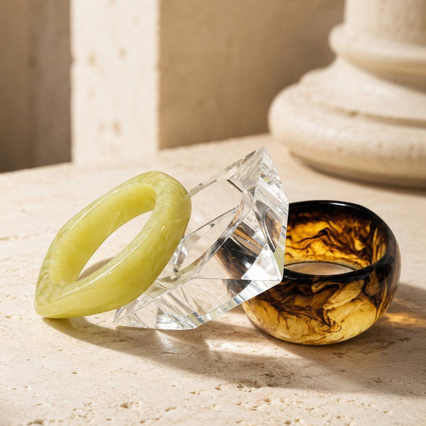 Three stacked resin bangles on travertine surface near stone column in natural light