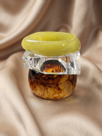 Tortoiseshell, clear faceted, and lime green resin bangles stacked upright on cream satin fabric