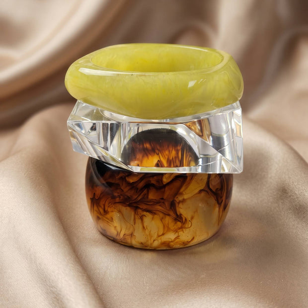 Tortoiseshell, clear faceted, and lime green resin bangles stacked upright on cream satin fabric