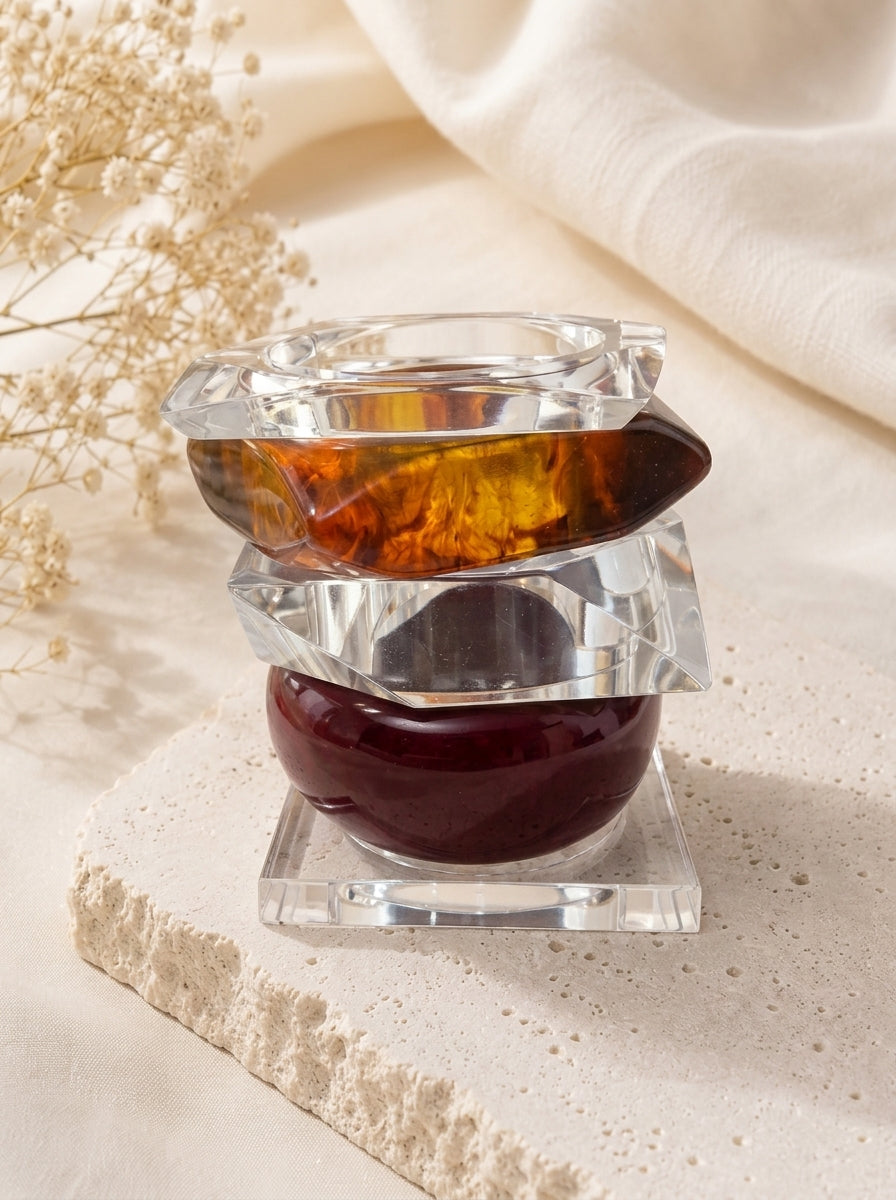 Three stacked acrylic and resin bangles on a stone riser with dried white flowers in the background