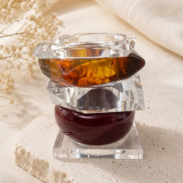 Three stacked acrylic and resin bangles on a stone riser with dried white flowers in the background