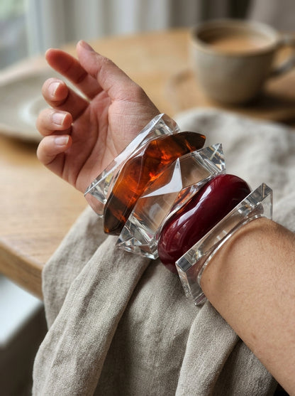 Two acrylic and resin bangles worn together on a wrist against a linen fabric background