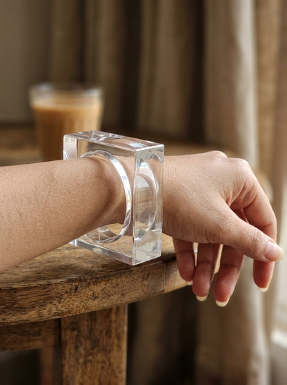Clear acrylic square bangle worn on a woman's wrist resting on a wooden table edge