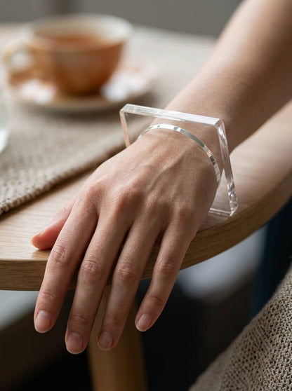 Clear acrylic square bangle worn on a woman's wrist resting on a wooden table beside a tea cup