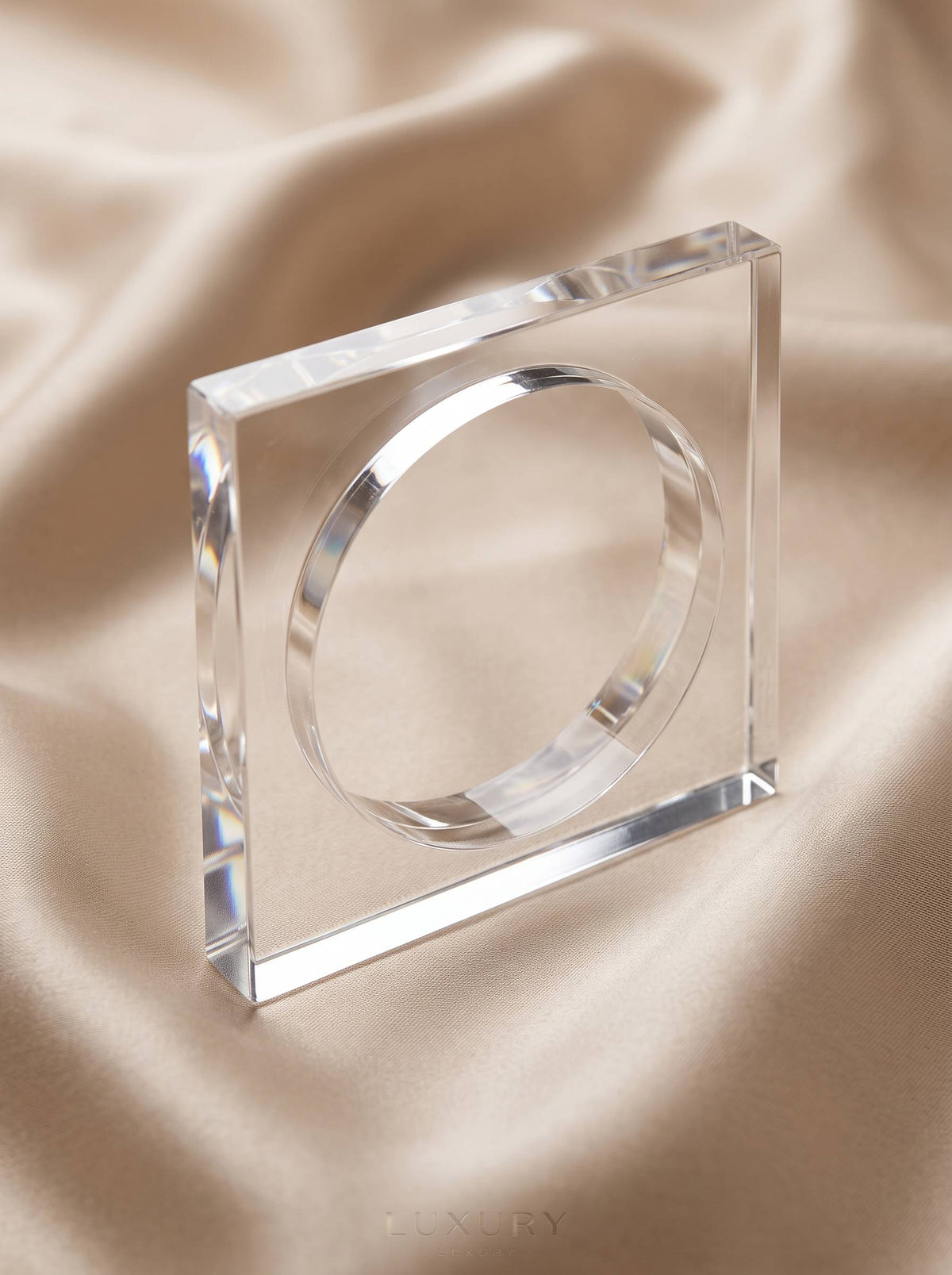 Close-up of clear acrylic square bangle standing on champagne satin fabric showing bevelled edges and light refraction