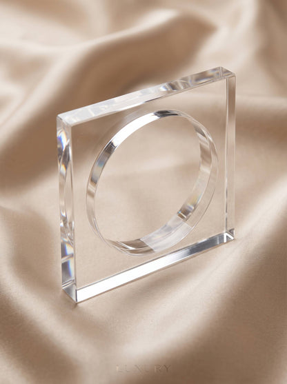 Close-up of clear acrylic square bangle standing on champagne satin fabric showing bevelled edges and light refraction