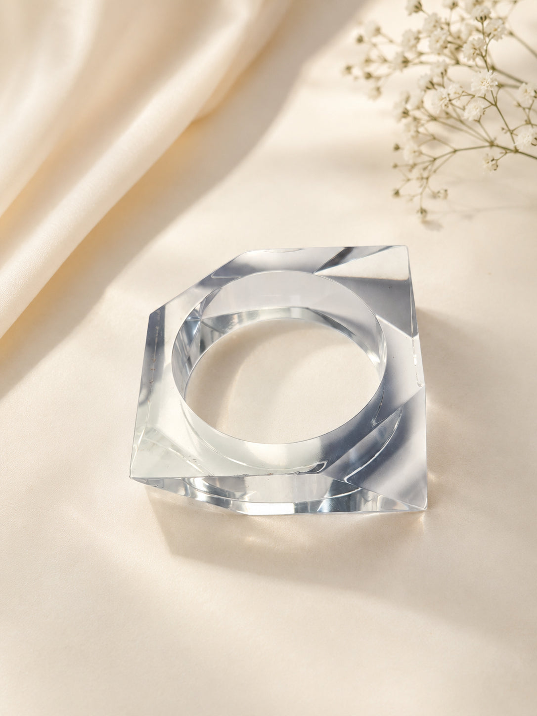 Transparent acrylic square bangle lying flat on ivory satin fabric with gypsophila flowers in background