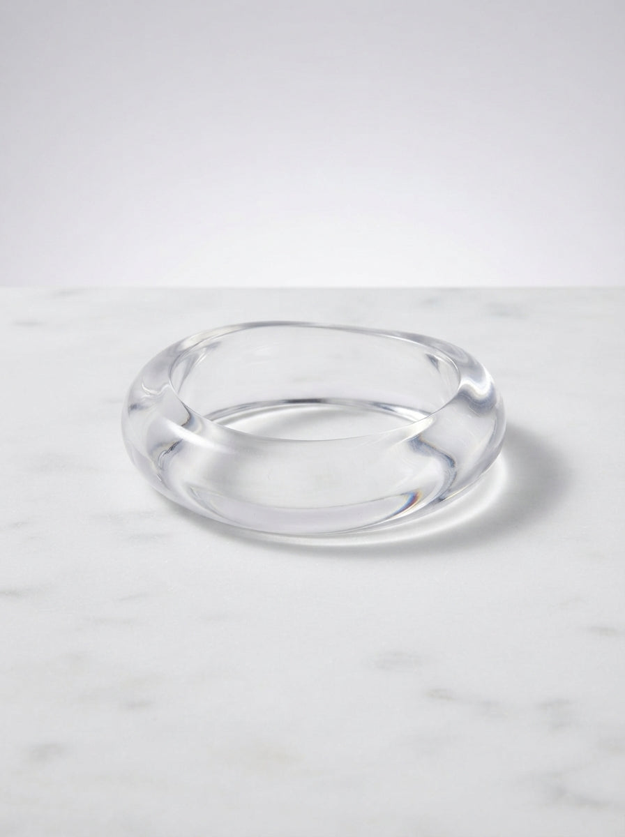 Transparent acrylic bangle with a rounded profile resting on a white marble surface showing its glossy finish