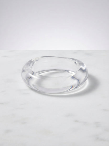 Transparent acrylic bangle with a rounded profile resting on a white marble surface showing its glossy finish