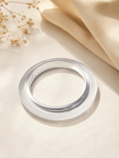 Clear transparent acrylic bangle lying flat on a cream surface with dried flowers in background