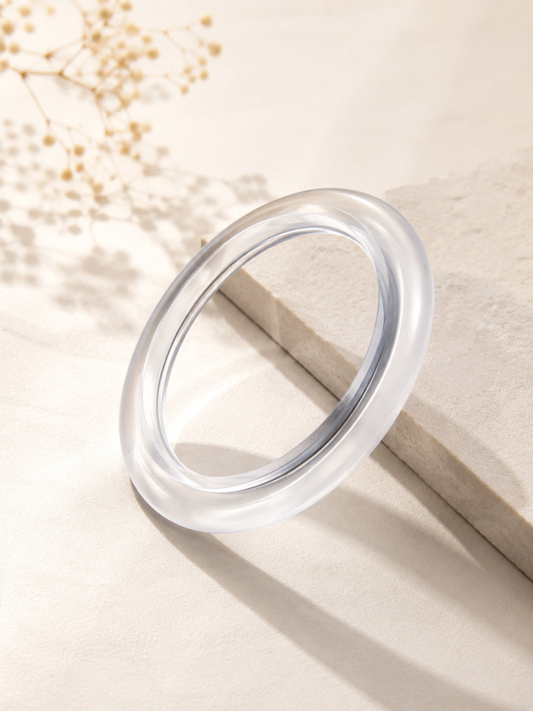 Clear acrylic bangle leaning upright against a stone block with soft dappled shadows