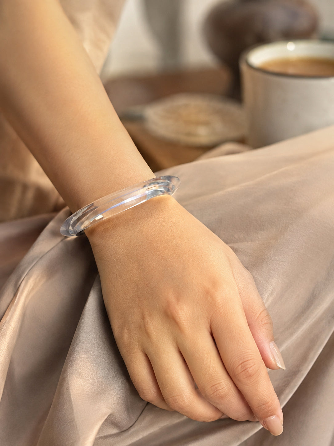 Clear acrylic bangle worn on a woman's wrist against a satin fabric background