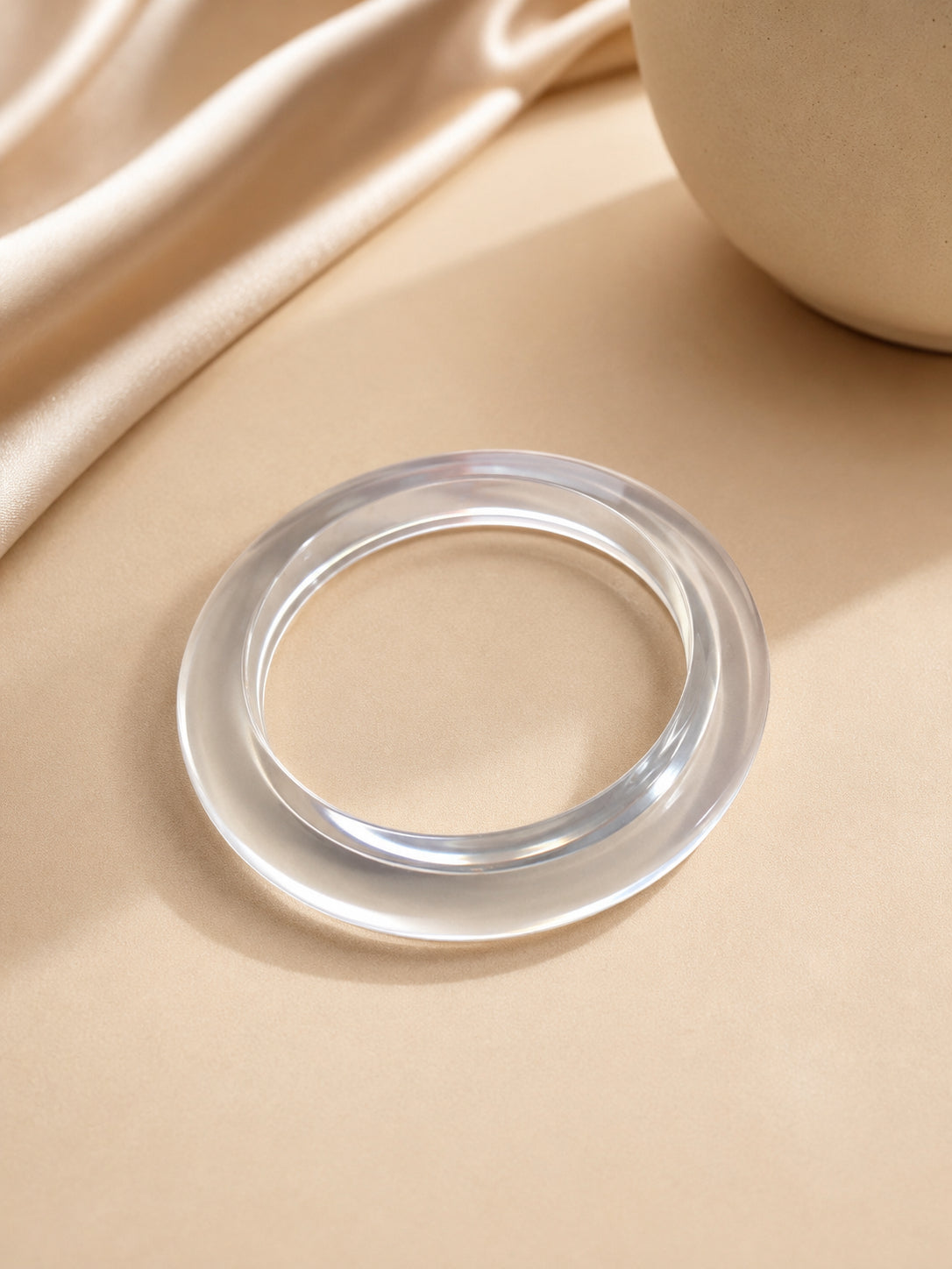 Clear transparent acrylic bangle placed flat on a golden satin cloth surface