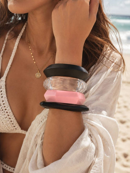 Model wearing four stacked black, clear and pink acrylic bangles at a sandy beach